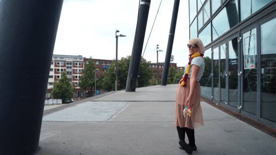 Mädchen mit weißen Haaren steht mit zwei kleinen Kuscheltieren und einem langen Spitzenrock vor Säulen.